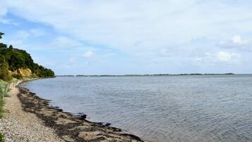 A coastal landscape with a pebble beach, calm water, and a distant island.