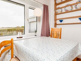 Una habitación con una cama, un ventanal con vista a un campo, un estante de madera con platos y una lámpara colgante.