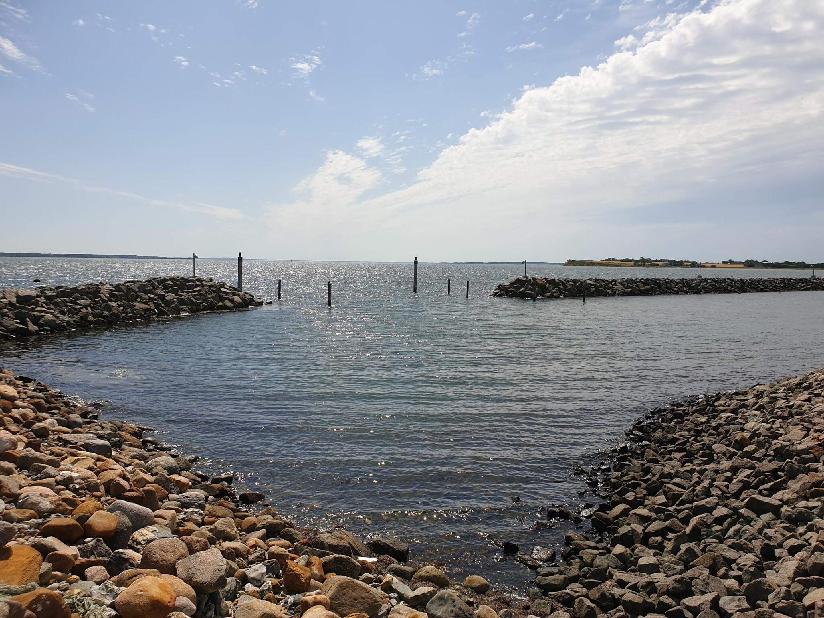 Un rivage rocheux bordé d’une eau calme, un ciel dégagé et une terre lointaine à l’horizon.