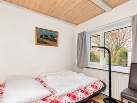 A bedroom with a bed, a window with curtains, a radiator, and a painting on the wall.