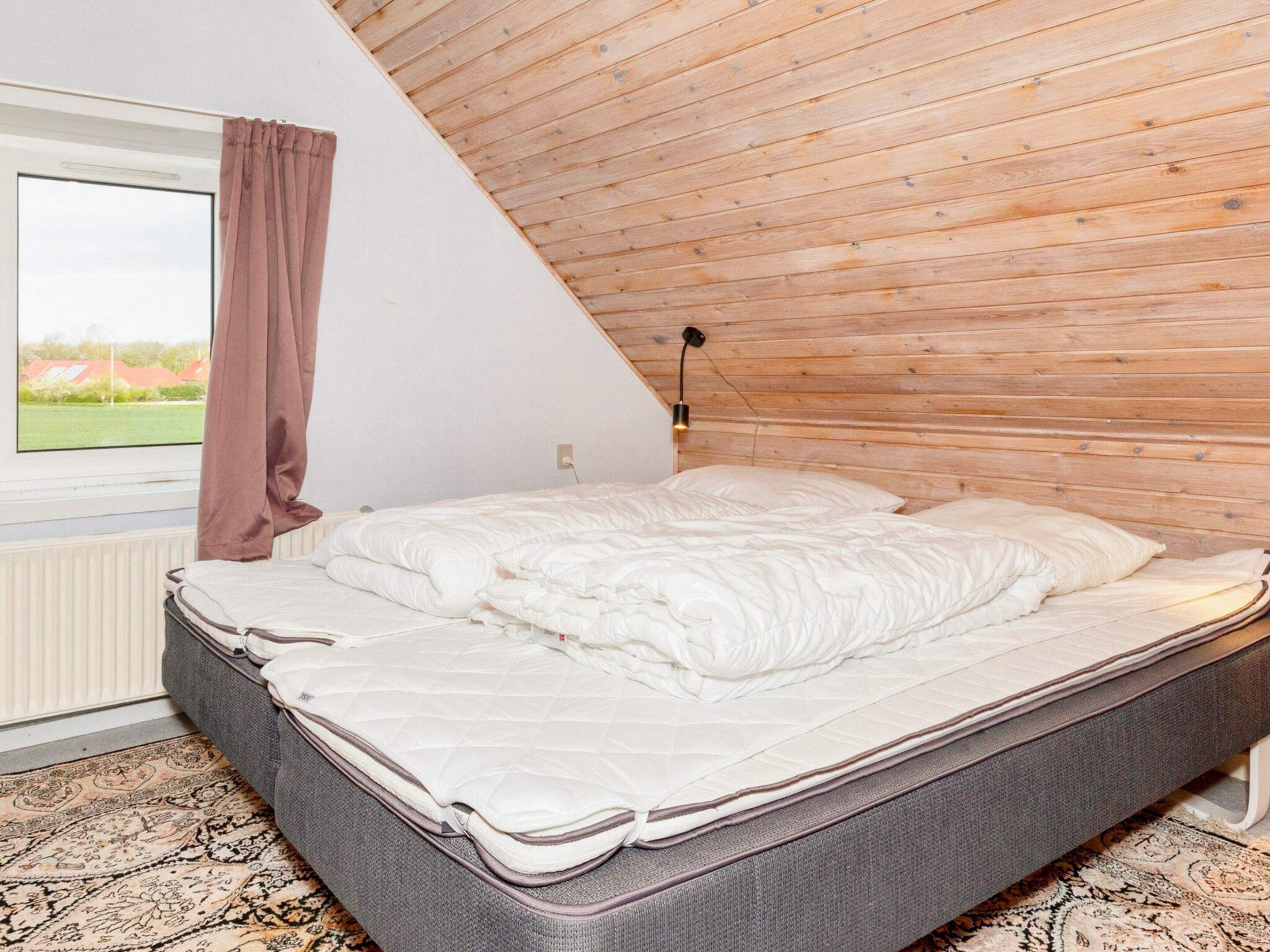 Une chambre avec un plafond en pente, un lit, une fenêtre donnant sur un beau paysage et une lampe fixée au mur.