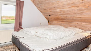Une chambre avec un plafond en pente, un lit, une fenêtre donnant sur un beau paysage et une lampe fixée au mur.