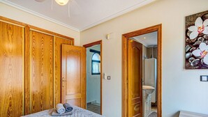 Quarto com cama grande, guarda-roupa de madeira e banheiro visível por uma porta aberta.