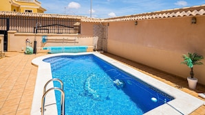 Piscina com deck azulejado, escada de metal e uma pequena planta.