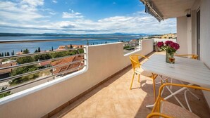 Un balcone con tavolo bianco e sedie gialle, vista su uno specchio d'acqua e montagne in lontananza.