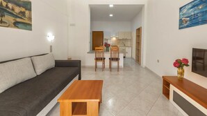 Un soggiorno con divano, un tavolino in legno e un mobile TV. Si nota un'area pranzo con tavolo e sedie. Lo sguardo si perde sulla cucina sullo sfondo.