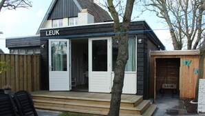 A modern house with a 'LEUK' sign, a wooden deck, and a small garden area. - Holiday Home Leuk Comfortable Vacation Home (Callantsoog)