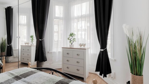 Une chambre à coucher avec un lit, une commode et une fenêtre ornée de rideaux légers.