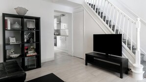 Un salon moderne avec un meuble de rangement noir pour l’équipement audiovisuel, un escalier blanc et une bibliothèque.