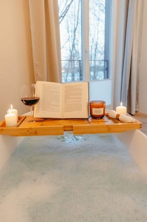 A wooden tray with a book, a candle, and a glass of red wine on a bathtub.