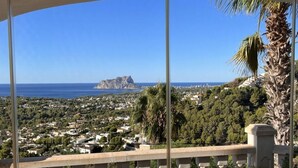A balcony with a view of a coastal town, a prominent rocky island, and dense greenery. - Villa Miraflores Comfortable Holiday Residence (Teulada)