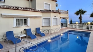 A poolside area with a pool, blue lounge chairs, and a building with a tiled roof and windows. - Villa Miraflores Comfortable Holiday Residence (Teulada)