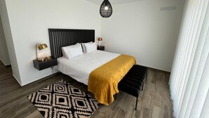 Una camera da letto moderna con un letto, comodini, un tappeto decorato, una panca e una lampada a sospensione.