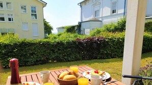 A breakfast table with plates of food, glasses of orange juice, and a bottle of wine, set on a wooden table outdoors with buildings in the background. - Holiday Apartment sea bay (Sassnitz)