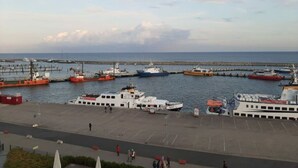 A marina with several boats docked, a pier extending into the water, and a paved walkway with people walking. - Holiday Apartment sea bay (Sassnitz)