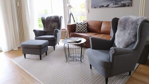 A modern living room with a brown leather sofa, grey armchairs, and a small round table. - Holiday Apartment sea bay (Sassnitz)