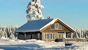A wooden cabin with a snow-covered roof, surrounded by snow-covered trees and hills. - 8 Person Holiday Home in Osen (Åmot)