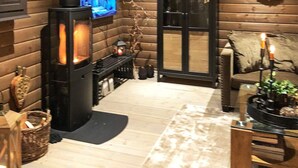 A cozy log cabin interior with a wood-burning stove, a television mounted on the wall, and a comfortable seating area with a cushioned chair and a small table. - 8 Person Holiday Home in Osen (Åmot)