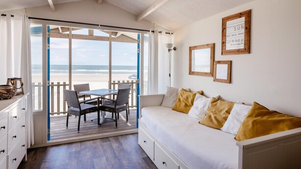 Une chambre avec un lit, une table entourée de chaises, une vue sur la plage et un plafond en bois.