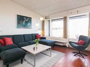 Una sala de estar moderna con un sofá gris oscuro, un sillón a juego, una mesita con un jarrón de flores y un ventanal con cortinas.