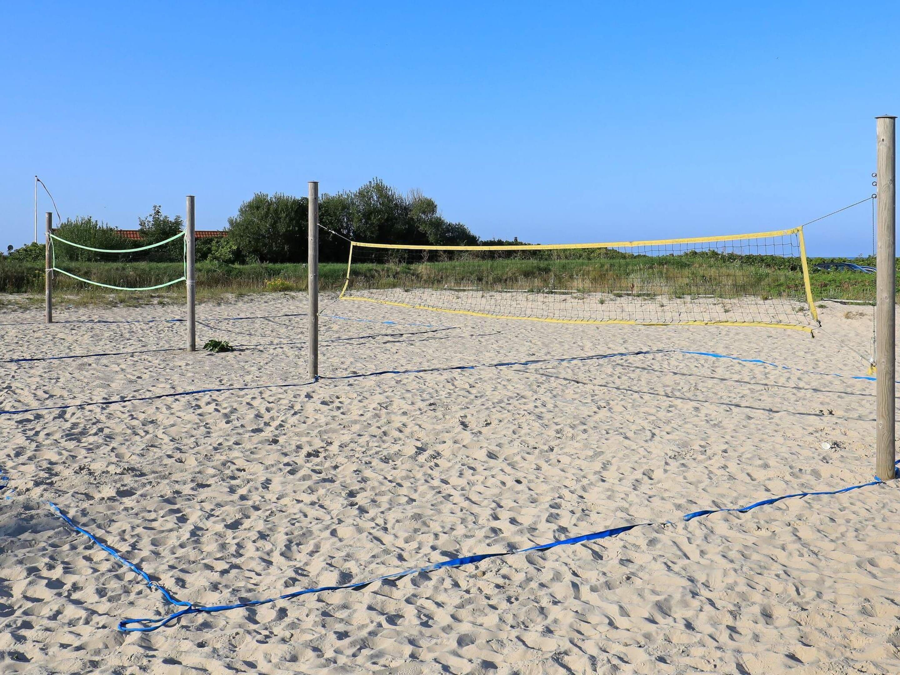 Ein Beachvolleyballfeld mit Netz und Pfosten, umgeben von Sand und Vegetation.