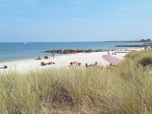 A beach with people sunbathing, a large red and white striped umbrella, and a rocky breakwater in the background. - 6 Person Holiday Park Home in Saeby (Sæby)