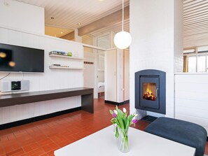A modern living room with a fireplace, a flat-screen TV mounted on the wall, and a white table with a vase of flowers.