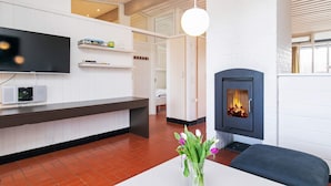 Ein modernes Wohnzimmer mit Kamin, einem flachbildfernseher an der Wand und einem weißen Tisch mit Blumen.