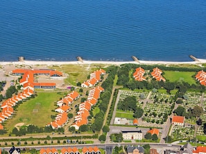 An aerial view of a coastal residential area with rows of houses, a beach, and a large building with a red roof. - 6 Person Holiday Park Home in Saeby (Sæby)