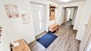 Un couloir avec un banc en bois, une porte, un radiateur et un porte-manteau suspendu.