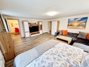 A modern living room with a flat-screen TV, a sofa, a coffee table, and a bed. - Beautiful Apartment Near Worthersee (Kottmannsdorf)