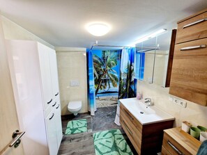 A bathroom with a toilet, sink, vanity, and a shower curtain with a tropical beach scene. - Beautiful Apartment Near Worthersee (Kottmannsdorf)