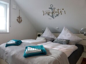 A bedroom with two beds, each with a teal and white towel, a wall-mounted anchor decoration, and a window to the left. - Inviting Apartment in Norden (Norden)