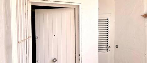 A white door with a metal handle, a small vent above it, and a window with horizontal blinds to the right.