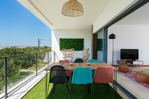 A balcony with a dining table, chairs, a TV, and a green wall. - Apartment Marina Sky (Lagos)