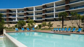 A pool area with blue lounge chairs and a multi-story building in the background. - Apartment Marina Sky (Lagos)