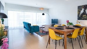 A modern living room with a blue sofa, yellow chairs, and a wooden dining table. - Apartment Marina Sky (Lagos)
