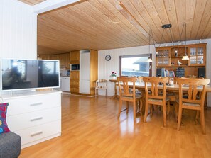 A spacious living area with a wooden ceiling, a dining table with chairs, a television, and a kitchen area with wooden cabinets and appliances. - 8 Person Holiday Home in Aabenraa (Aabenraa)