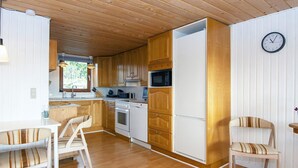 A compact kitchen with wooden cabinets, a white refrigerator, and a microwave. There are two chairs with striped cushions. - 8 Person Holiday Home in Aabenraa (Aabenraa)