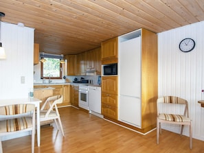 A compact kitchen with wooden cabinets, a white refrigerator, and a microwave. There are two chairs with striped cushions. - 8 Person Holiday Home in Aabenraa (Aabenraa)