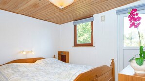 A bedroom with a wooden bed, a bedside table with a lamp, a window with a view of greenery, and a wall-mounted shelf. - 8 Person Holiday Home in Aabenraa (Aabenraa)