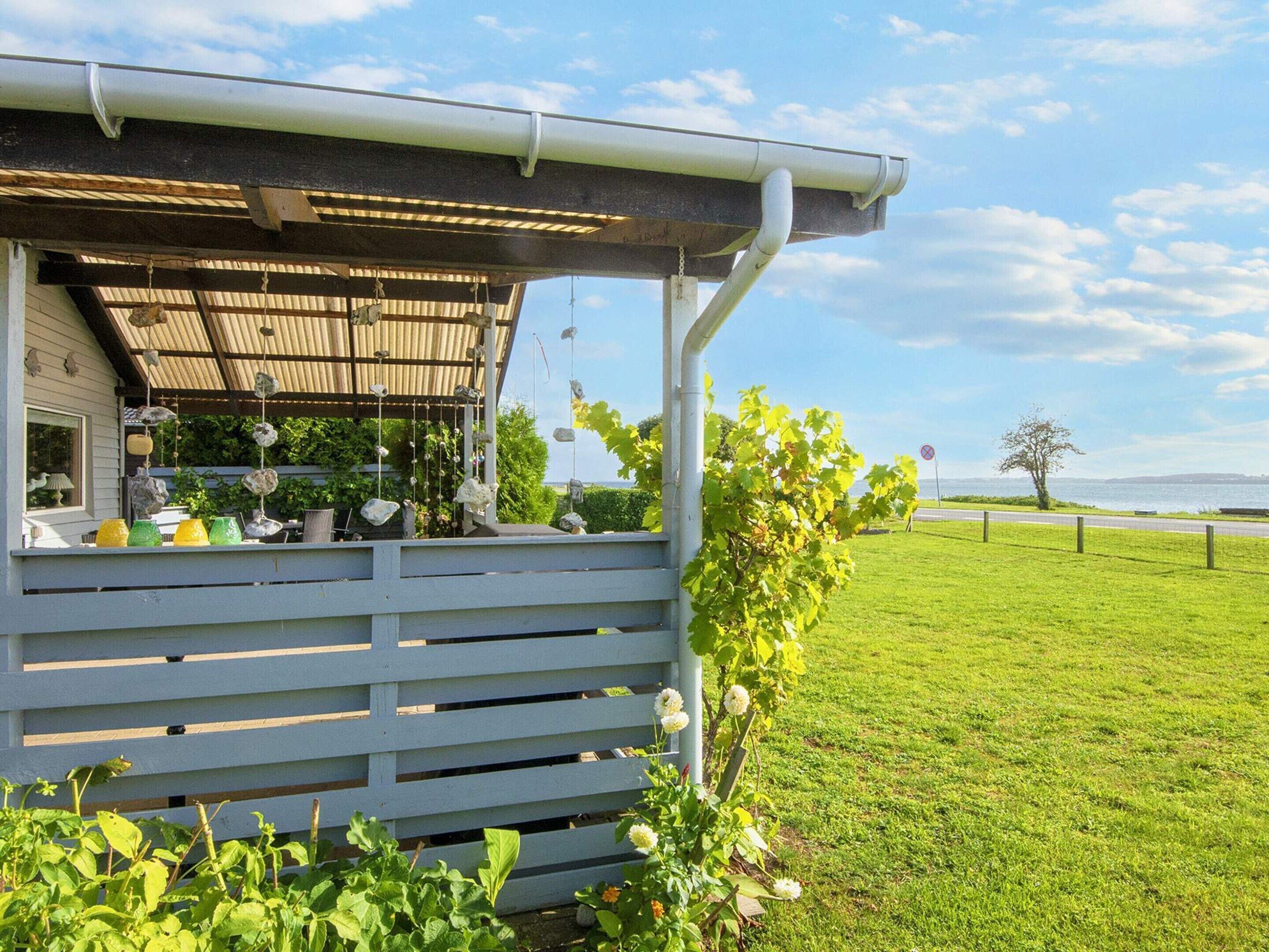 A covered outdoor area with a railing, a view of the sea, and a grassy field.