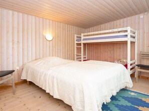 Une chambre avec un lit superposé, un lit simple, une chaise, une lampe fixée au mur et un tapis à motifs.