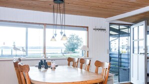 A dining area with a round wooden table, six chairs, and a view of a body of water through large windows. - 8 Person Holiday Home in Aabenraa (Aabenraa)