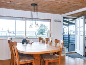 A dining area with a round wooden table, six chairs, and a view of a body of water through large windows. - 8 Person Holiday Home in Aabenraa (Aabenraa)