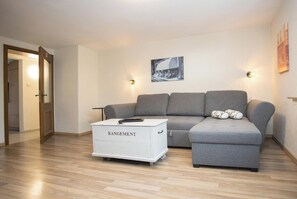 Una sala de estar moderna con un sofá gris, un mueble de almacenamiento blanco con la etiqueta 'RANGEMENT' y un aplique de pared.