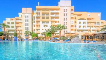 Un hotel amb piscina, diversos balcons i palmeres.