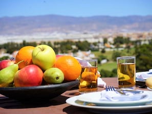 A table with a bowl of fruit, two glasses of tea, and a plate with cutlery.