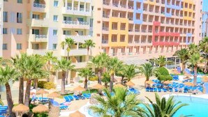 A multi-story hotel with balconies, a swimming pool, and palm trees. - Belvilla by OYO Apartamento 2 Dormitorios (Roquetas de Mar)