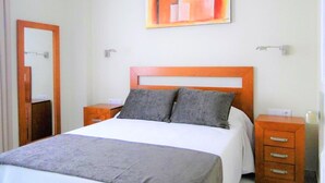 A bedroom with a bed, a nightstand, a drawer, a mirror, and a painting on the wall. - Belvilla by OYO Apartamento 2 Dormitorios (Roquetas de Mar)